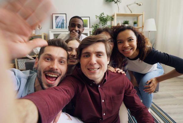 Gruppo di giovani si scatta un selfie. Sono 6 persone, in abiti casual, in primissimo piano si vedono le mani e il braccio di chi scatta la foto, poi i visi del gruppo.